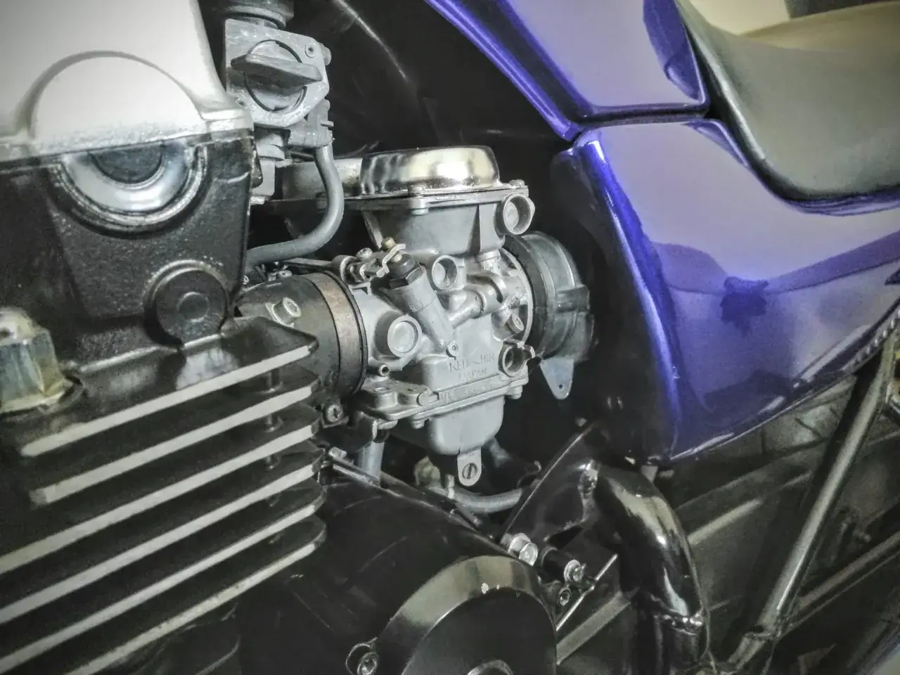 Silnik motocykla z gaźnikiem. Widoczna dysza wolnych obrotów, żebrowany cylinder i fioletowy bak.