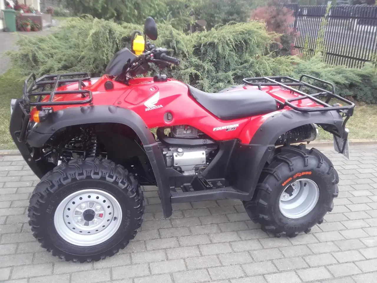 Czerwony quad Honda TRX 350 Fourtrax z czarnymi bagażnikami i terenowymi oponami, gotowy na przygodę.