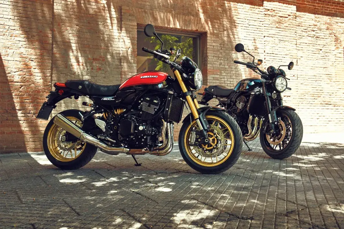 Dwa motocykle Kawasaki Z900RS w klasycznym stylu, jeden czerwono-czarny, drugi czarny, stoją przed ceglaną ścianą.