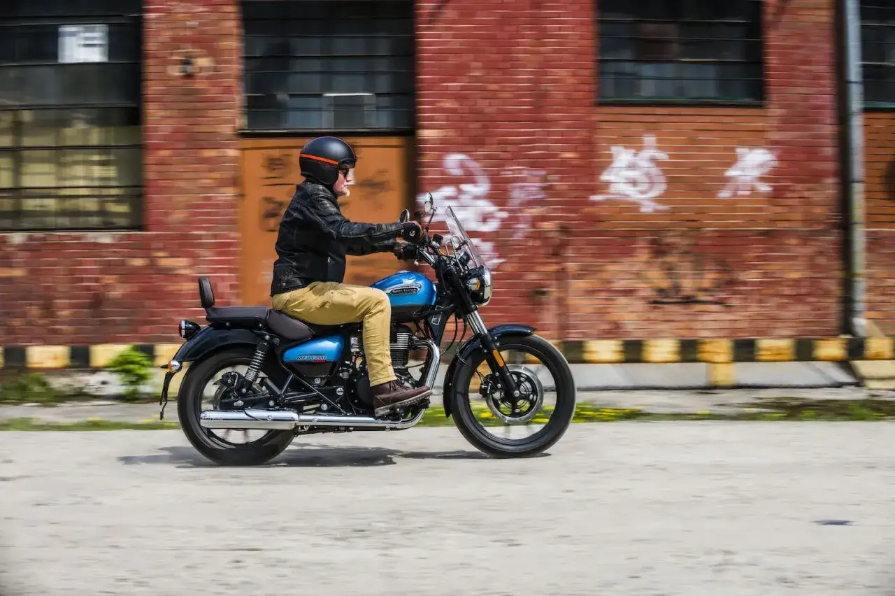 Mężczyzna w kasku i skórzanej kurtce jedzie na niebieskim motocyklu Royal Enfield Meteor 350.