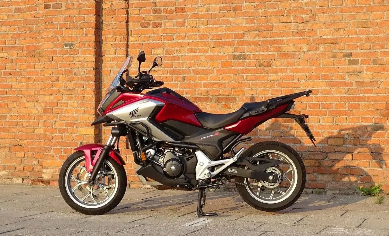 Czerwono-srebrny motocykl Honda NC750X na tle ceglanej ściany. Sprawdź aktualną honda nc750x cena!