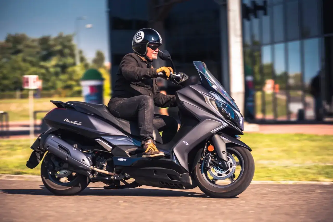 Mężczyzna w kasku jedzie na skuterze Kymco Downtown 125. Poznaj kymco downtown 125 dane techniczne i poczuj wolność.