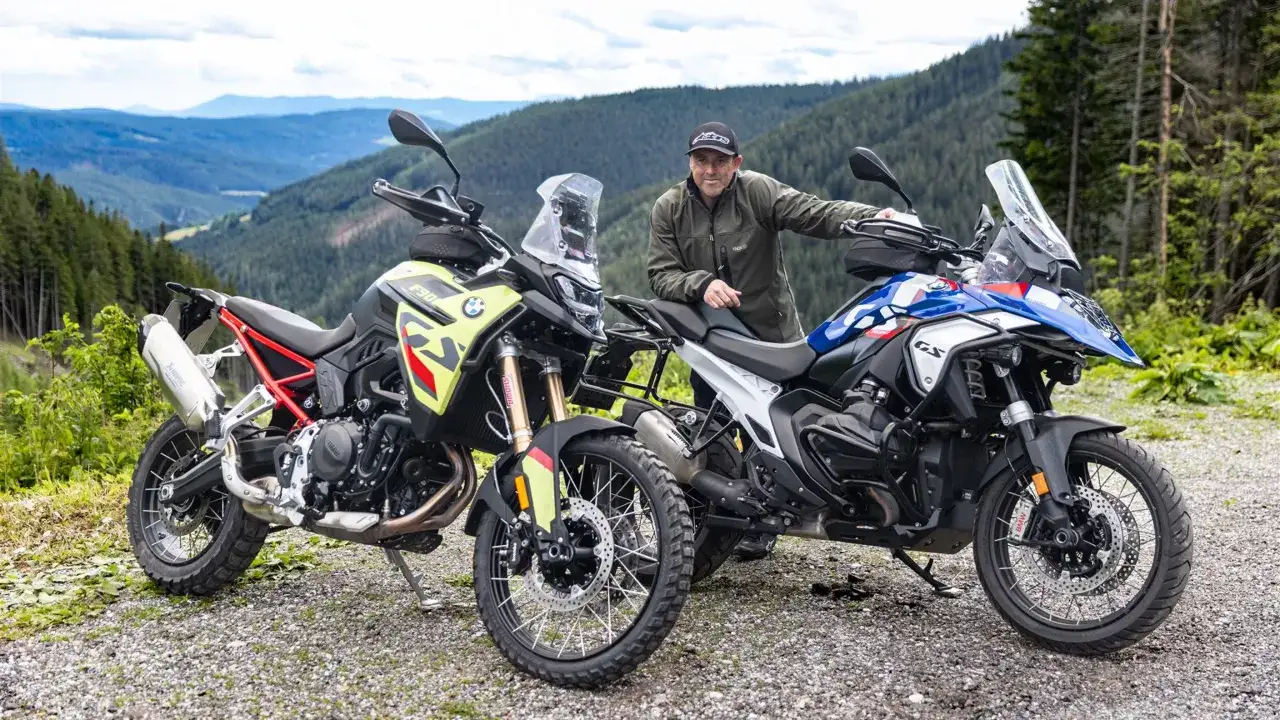 Mężczyzna opiera się o motocykl BMW R1300GS, obok stoi inny motocykl. Tło to górzysty krajobraz.