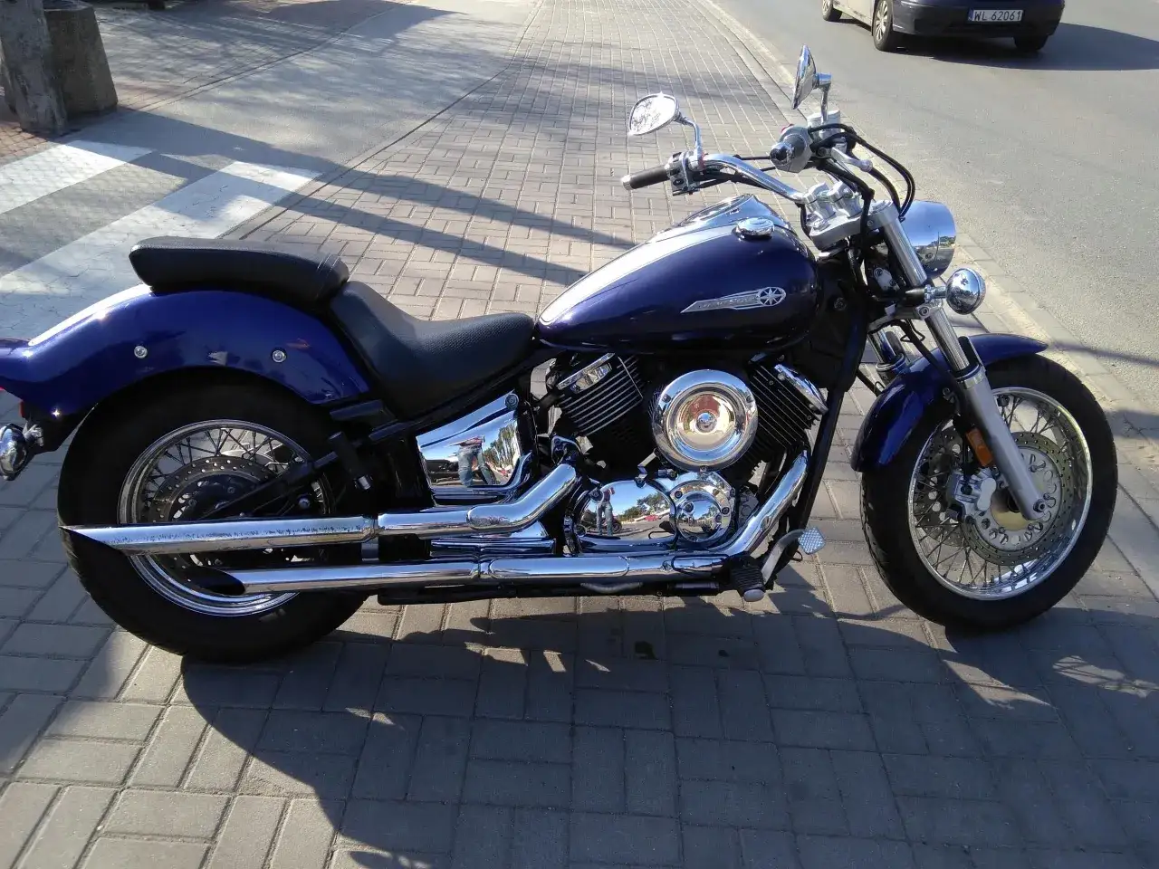 Błękitny motocykl Yamaha Drag Star 1100, z chromowanymi elementami, zaparkowany na chodniku. Dane techniczne tego klasyka są imponujące.