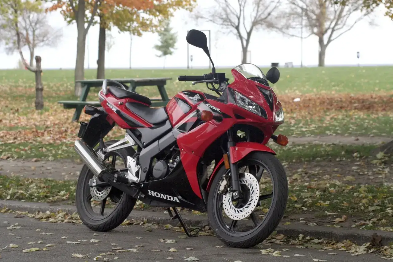 Czerwona Honda CBR 125 na tle jesiennego parku. Poznaj honda cbr 125 dane techniczne i możliwości tego sportowego motocykla.