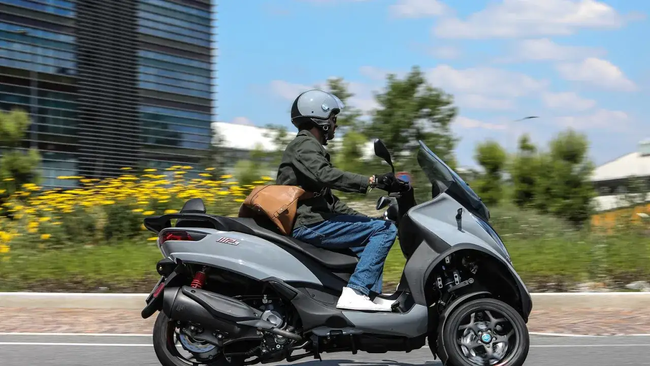 Mężczyzna w kasku jedzie na szarym Piaggio MP3 300. Poznaj piaggio mp3 300 dane techniczne i poczuj wolność.