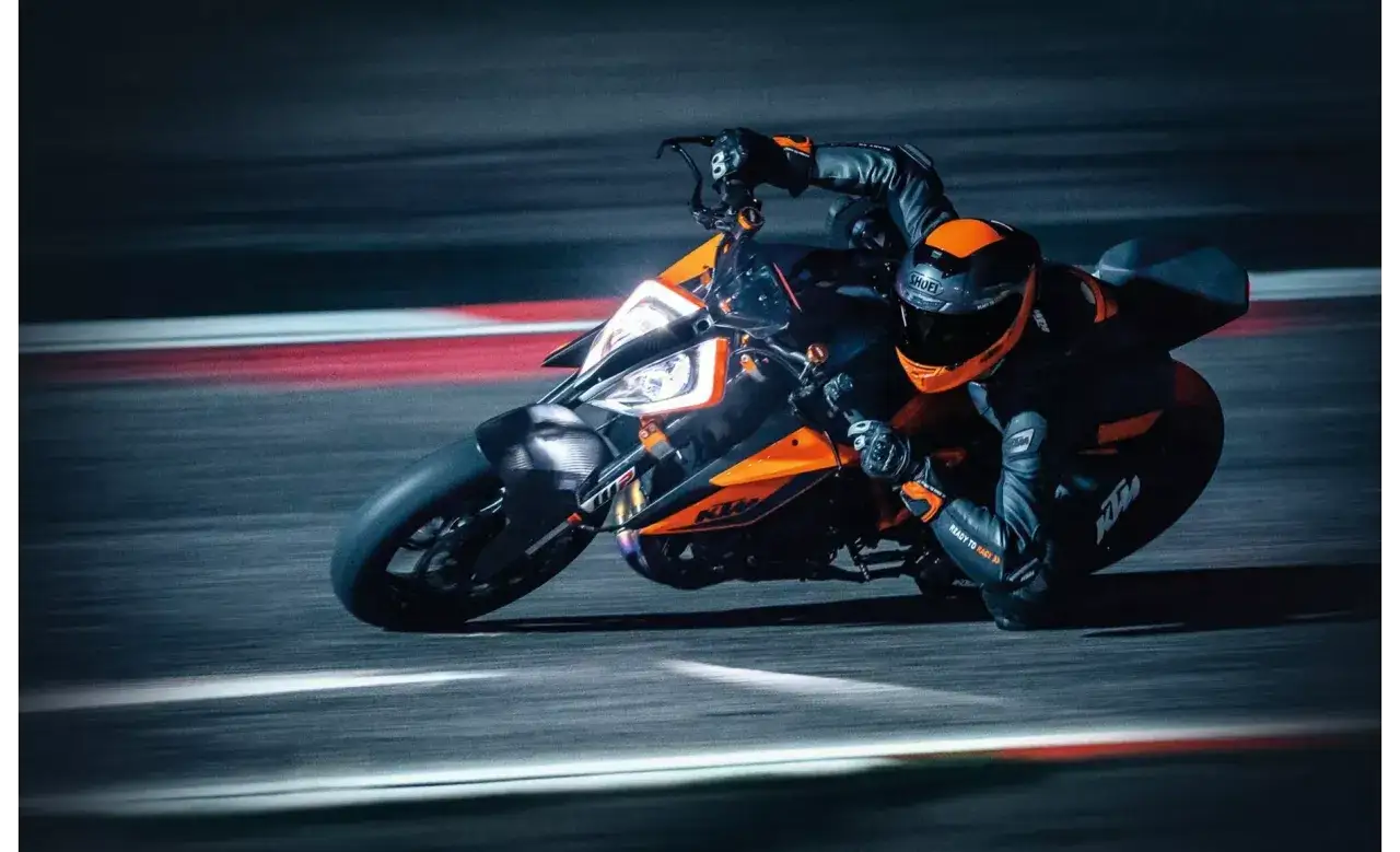 Motocyklista w kombinezonie i kasku ściga się na torze na pomarańczowo-czarnym motocyklu KTM 1290 Super Duke.