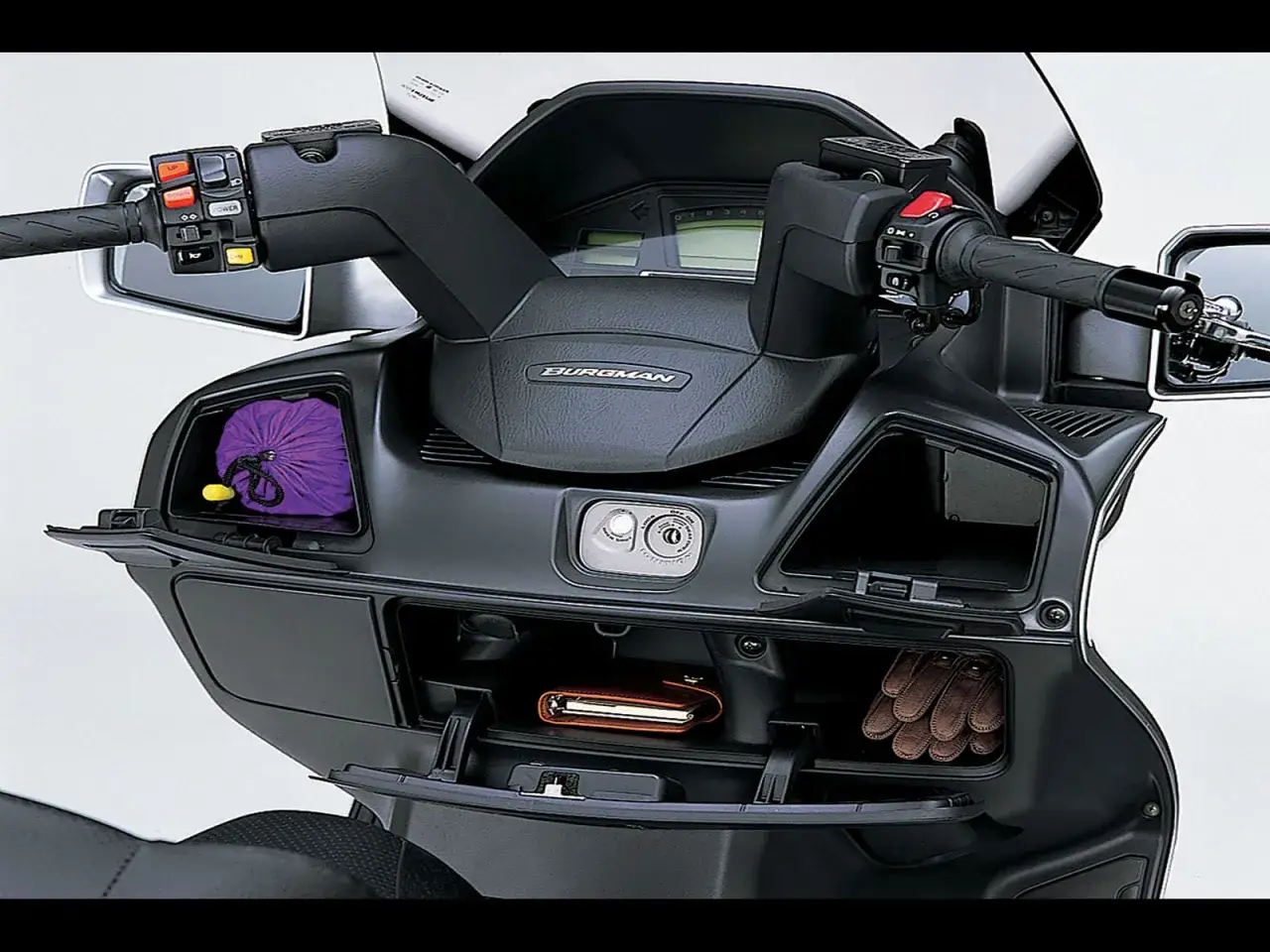 Suzuki Burgman 650 Executive z otwartymi schowkami: fioletowy worek, portfel i rękawiczki.