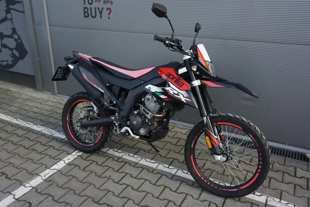 Czarny motocykl Aprilia RX 125 z czerwonymi akcentami i różowym siedzeniem, gotowy do jazdy. Sprawdź aprilia rx 125 dane techniczne.