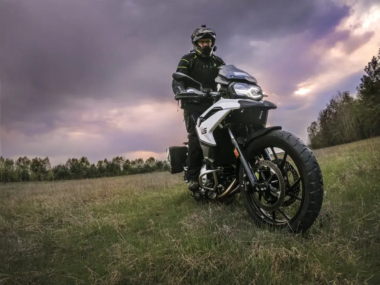 Motocyklista na motocyklu BMW F750GS w polu, pod burzowym niebem.