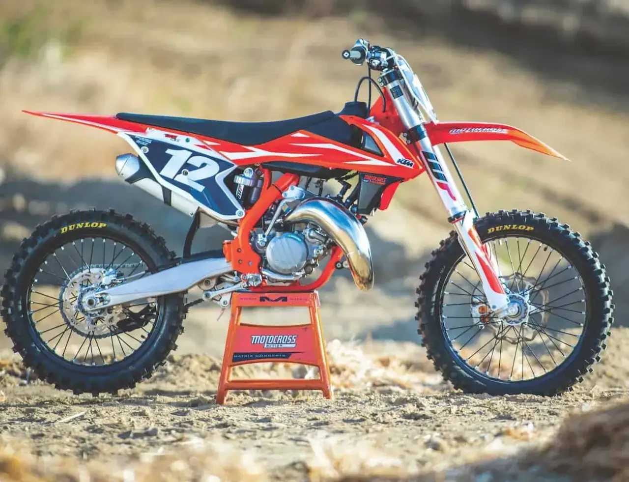 Pomarańczowy KTM SX 125 gotowy do osiągnięcia v-max na torze. Numer 12 na tabliczce.