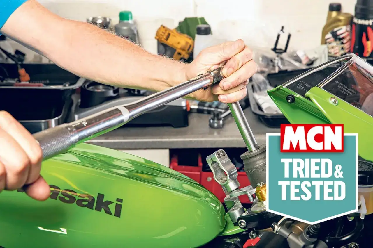 Ręce mechanika używają niutonometru do dokręcania śruby w zielonym motocyklu Kawasaki.