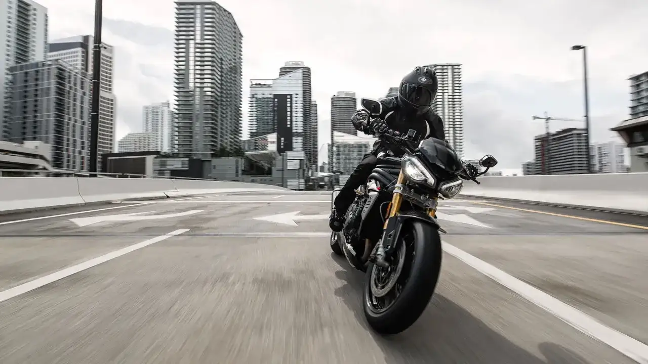 Motocyklista w kasku pędzi na Triumph Speed Triple 1050 przez miejską dżunglę.