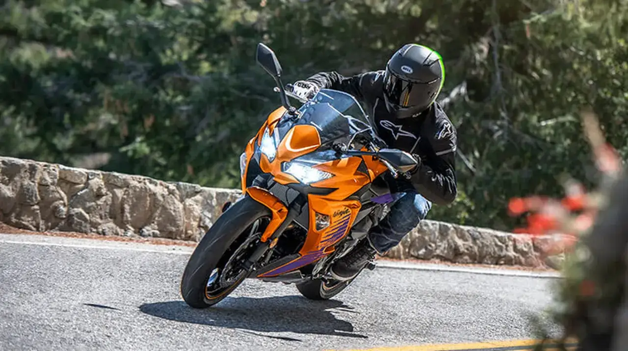 Motocyklista na pomarańczowym Kawasaki Ninja 650 pokonuje zakręt, sugerując jego potencjalną prędkość maksymalną.